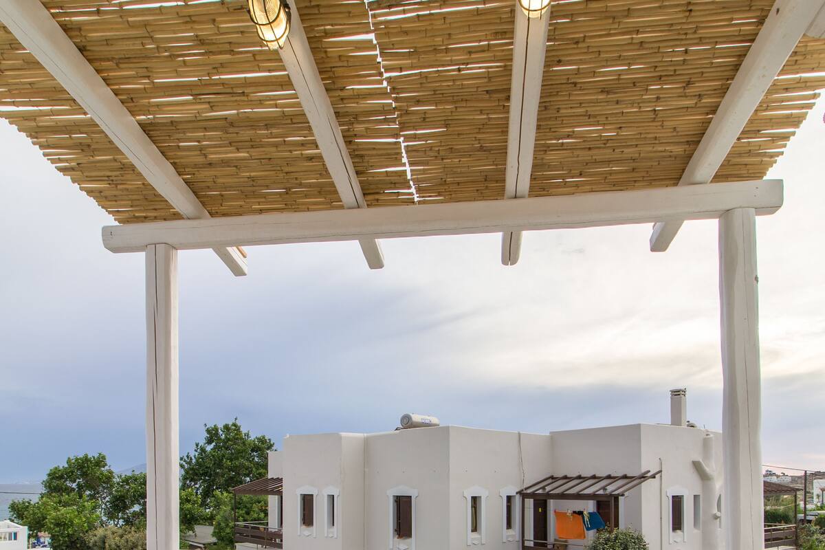 A covered outdoor seating area with a table and chairs, a view of buildings in the background, and a wooden ceiling.