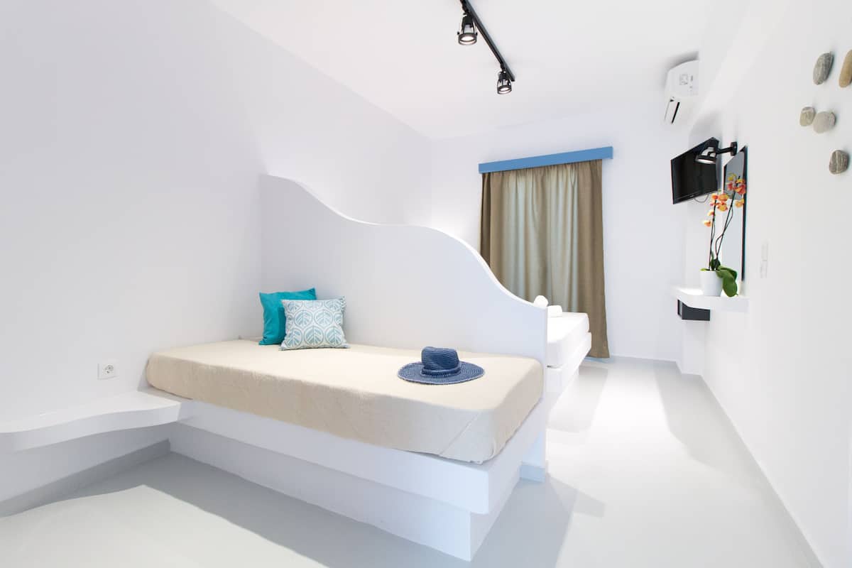 A modern, minimalist bedroom with a built-in bed, a small seating area, a wall-mounted TV, and a plant.
