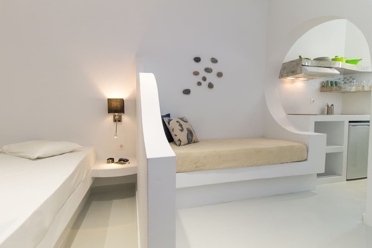 A modern, minimalist bedroom with a built-in bed, bedside table, and a small seating area.