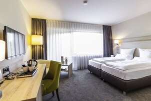 Habitación de hotel con cama, escritorio, silla, televisión y ventana con cortinas.