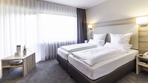 Hotelkamer met een tweepersoonsbed, nachtkastje, lamp en uitzicht op het buitenlandschap door dunne gordijnen.