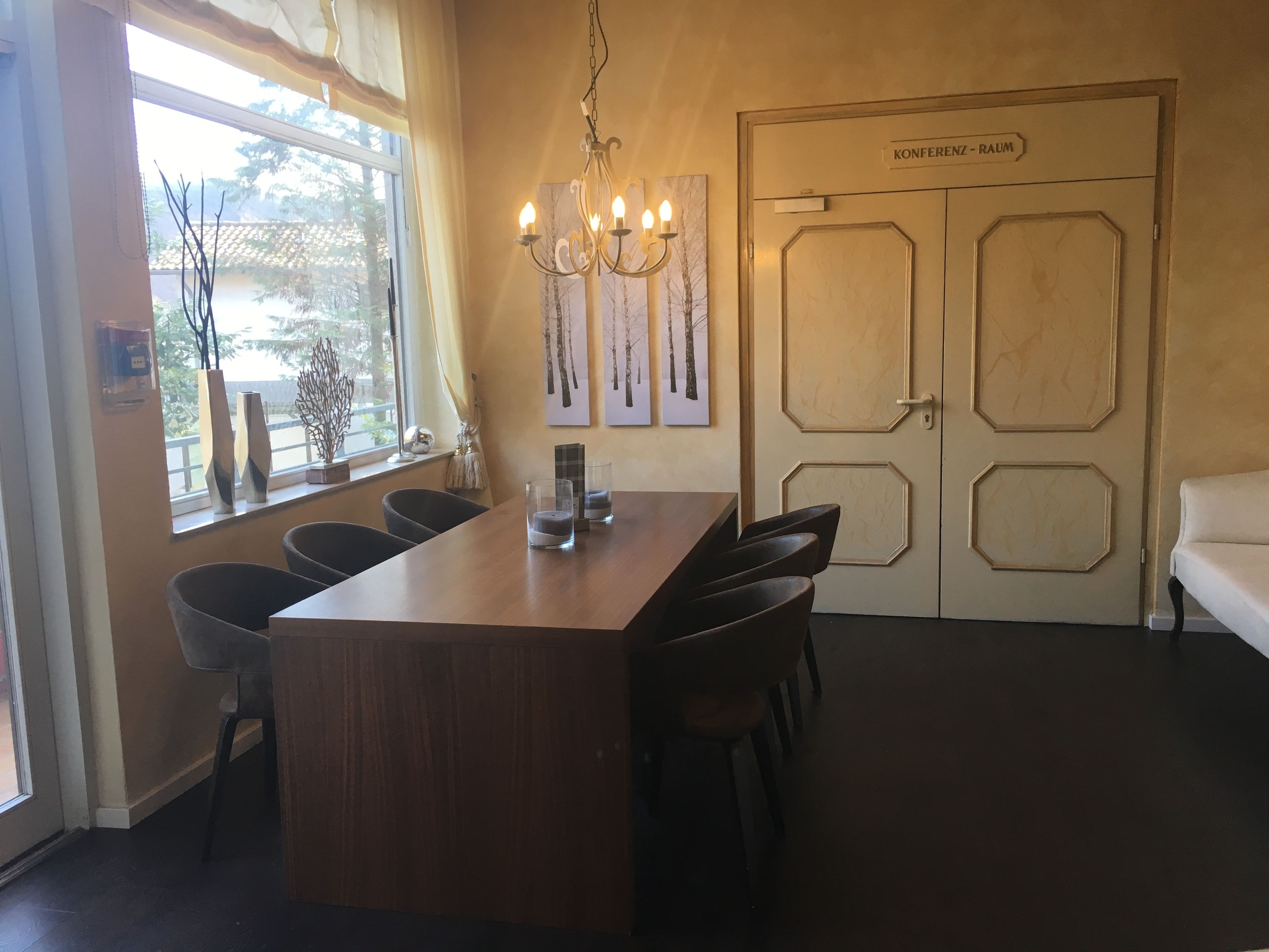 A conference room with a wooden table, chairs, a chandelier, and a door labeled "Konferenzraum".