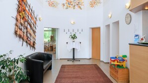 A hotel lobby with a high ceiling, a central table with a vase, a clock, and a children's play area. - Motel Hormersdorf (Schnaittach)