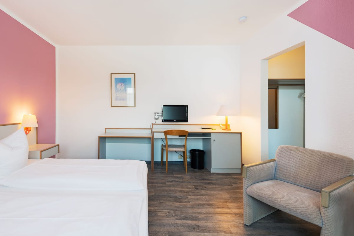A hotel room with a bed, desk, chair, and a television.