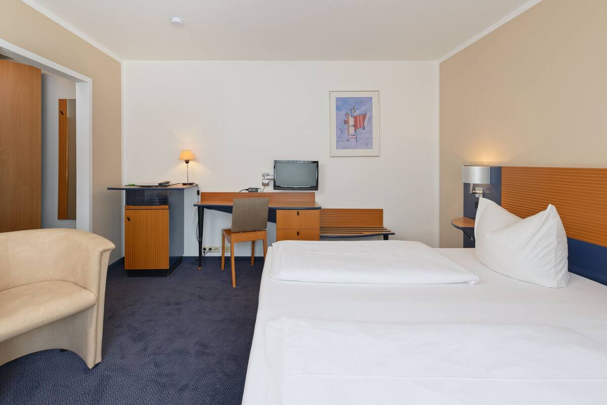 A hotel room with a bed, a desk, a chair, a television, and a small cabinet.