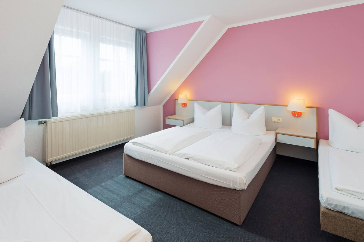 A modern hotel room with a large bed, a smaller bed, and a desk.
