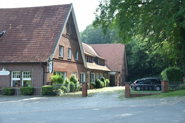 A traditional brick building with a steeply pitched roof, a gated driveway, and a parked car.