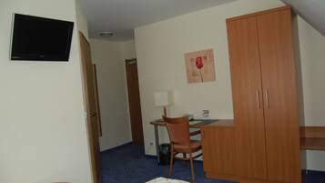 A hotel room with a bed, a desk with a chair, a television, a wardrobe, and a painting on the wall.