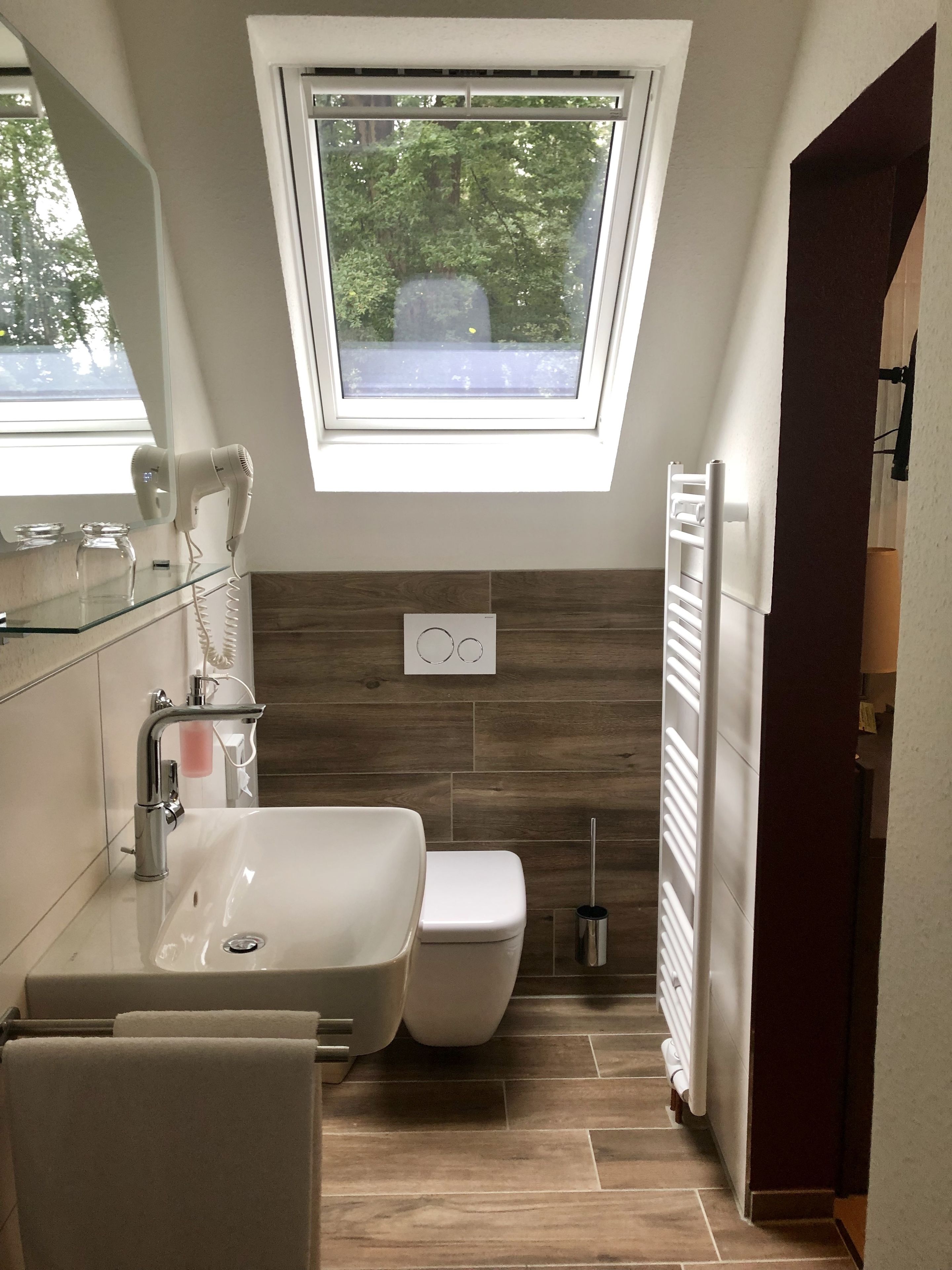 Ein modernes Badezimmer mit Dachfenster, einem weißen Waschbecken, einer Toilette und einem Handtuchhalter.