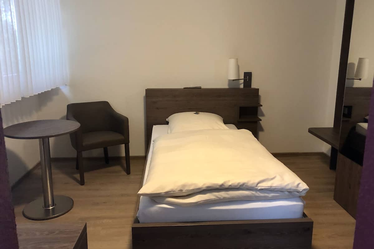 A single bed with a wooden headboard, a small round table, a chair, and a mirror.