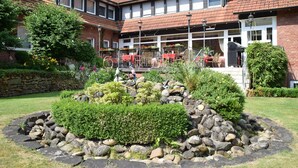 Un patio con jardín de piedra, mobiliario exterior y un edificio de ladrillo con múltiples ventanas.
