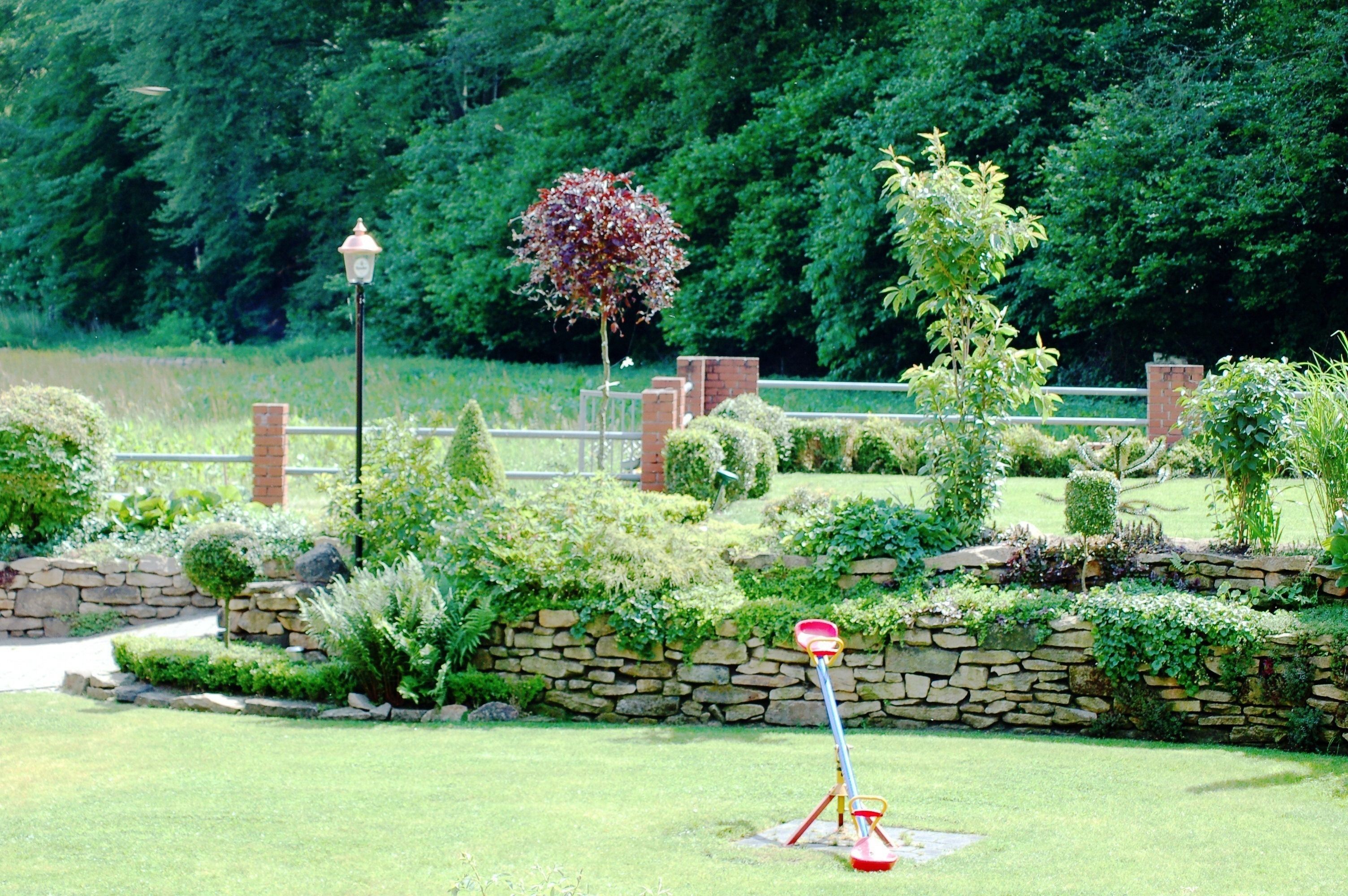 A well-maintained garden with a stone wall, various shrubs, and a lamp post.