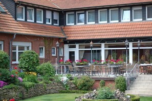 A two-story building with a brick facade, a tiled roof, and a patio area with outdoor seating.