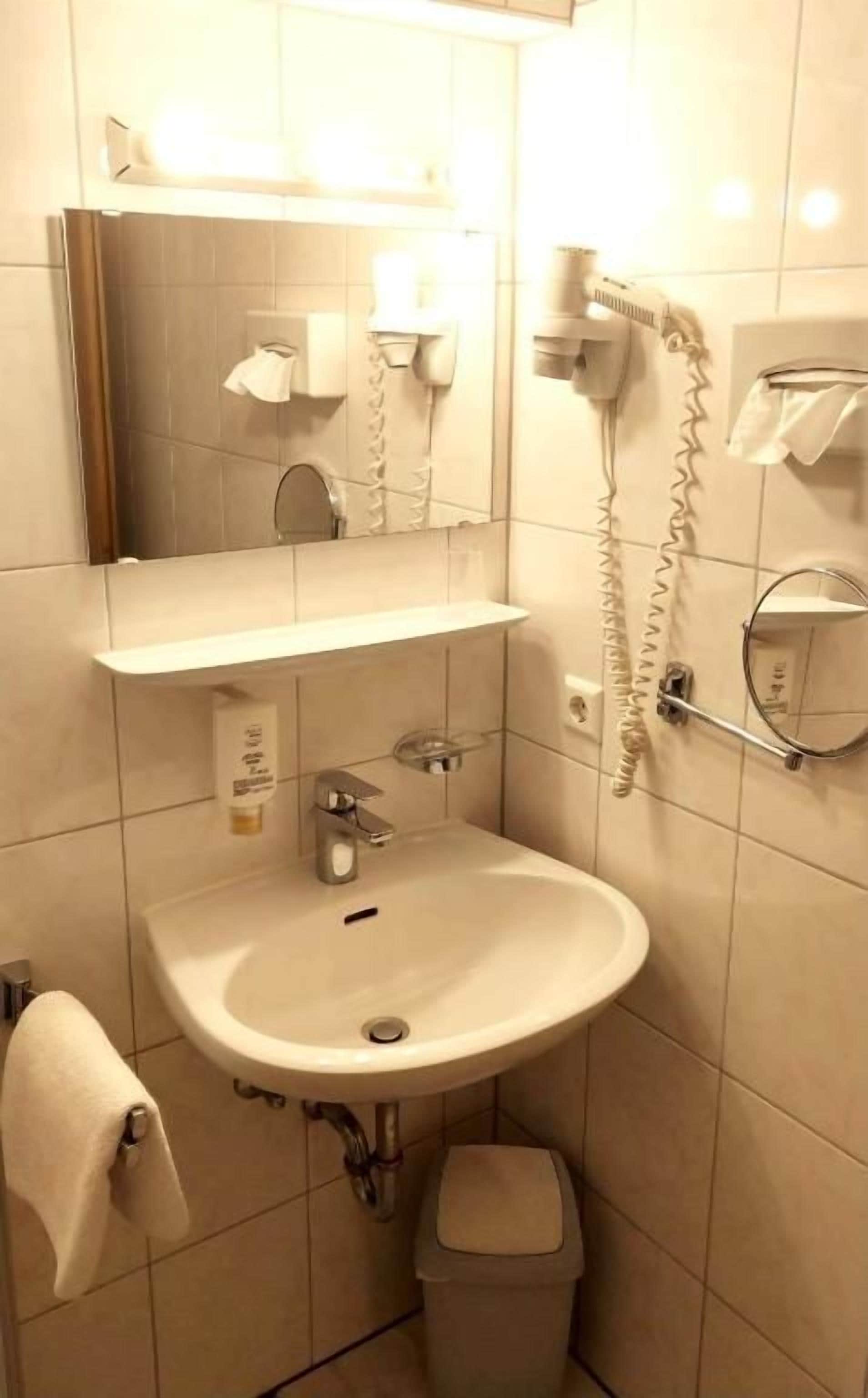 A bathroom with a sink, mirror, hairdryer, and towel rack.