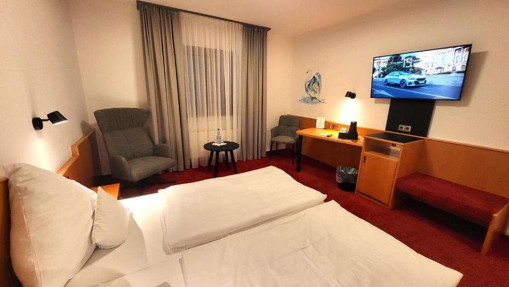 Una habitación de hotel con una cama, un escritorio, una silla, un televisor y un ventanal con cortinas.