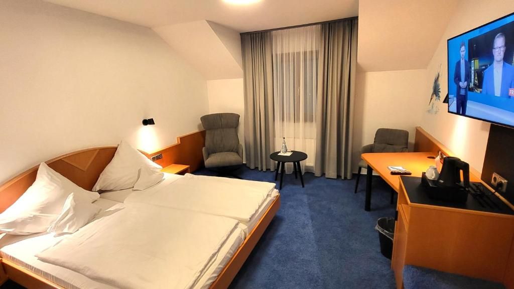 Habitación de hotel con cama, dos sillas, una mesita, televisor y ventana con cortinas.