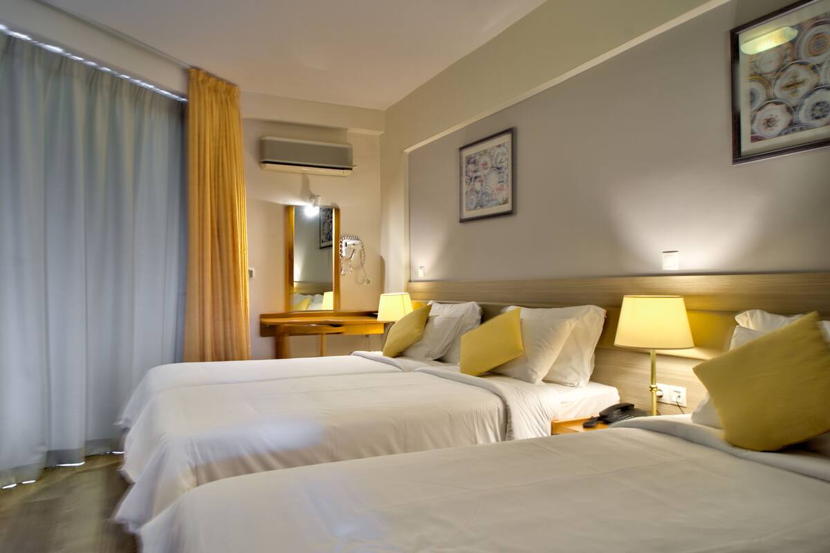 A hotel room with two beds, a bedside table with a lamp, a mirror, and a painting on the wall.