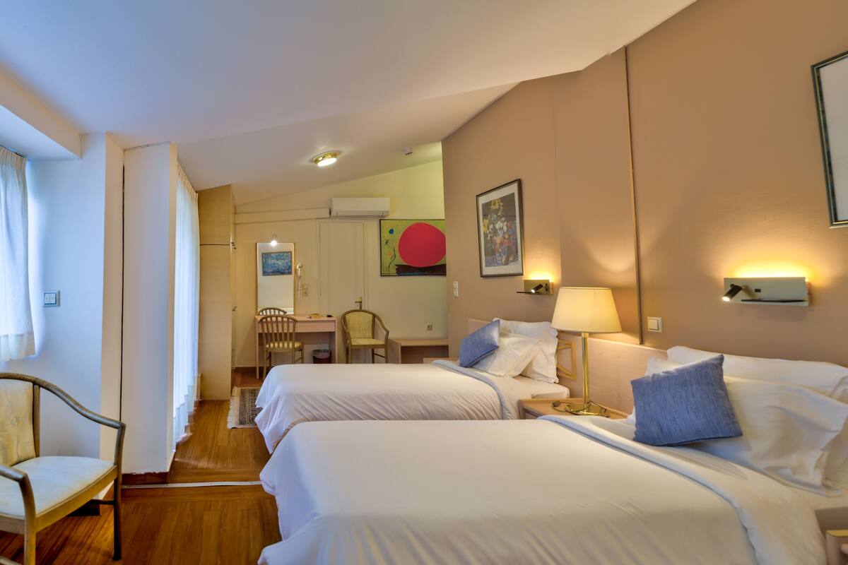 A hotel room with two beds, a desk, a chair, and a dining area.