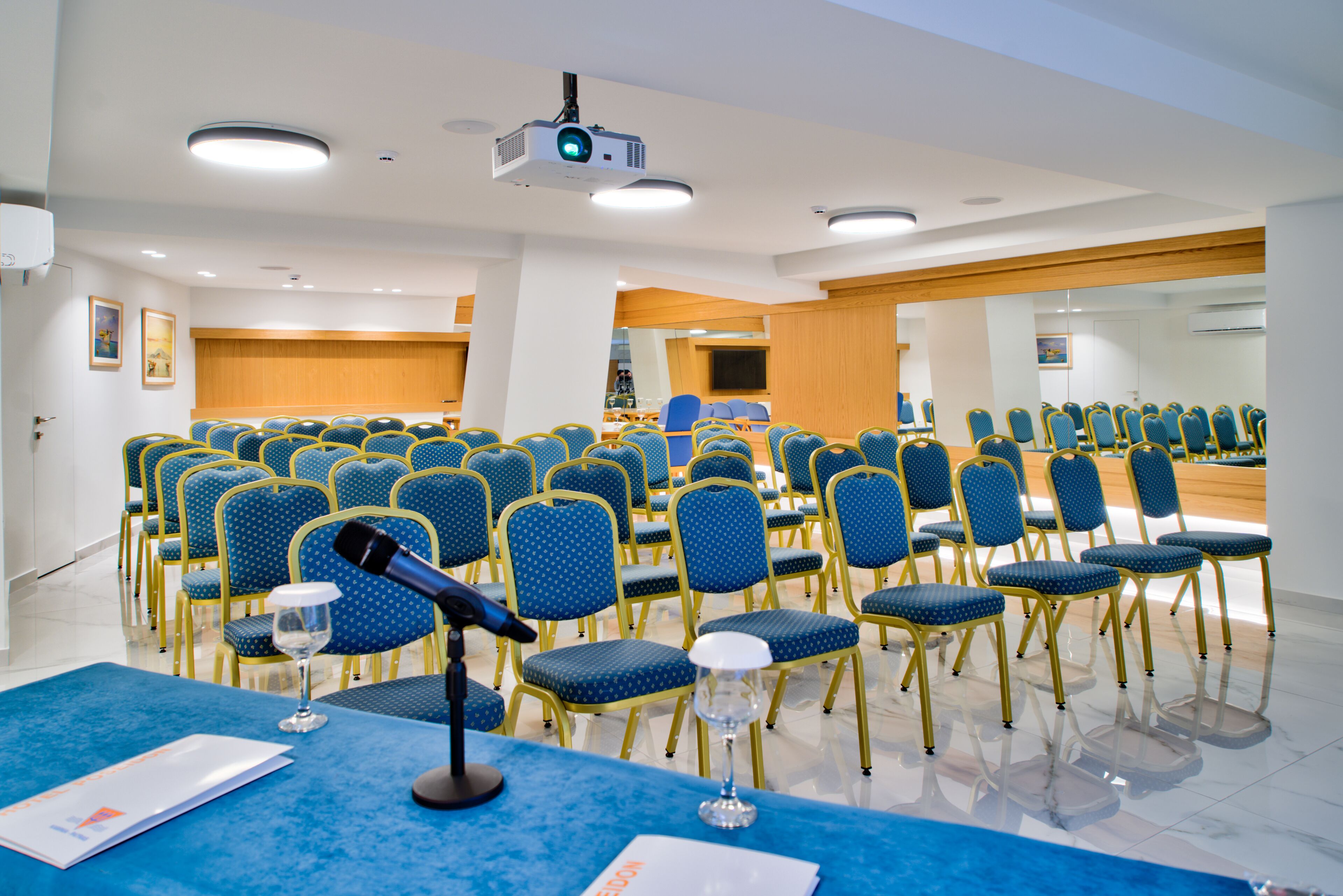 Un salón de conferencias con hileras de sillas azules, un atril y un proyector.
