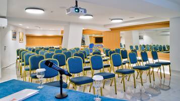 Un salón de conferencias con hileras de sillas azules, un atril y un proyector.