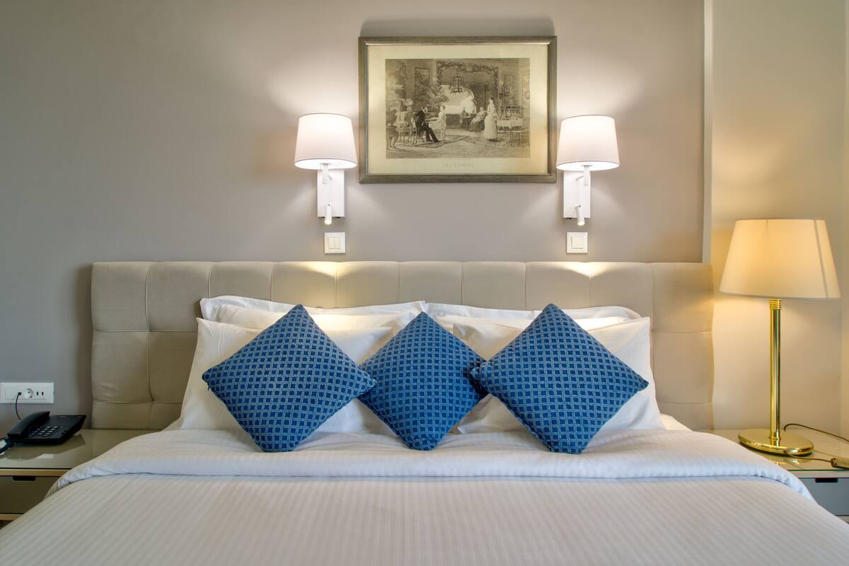 A hotel room with a large bed, two wall-mounted lamps, a framed picture above the bed, and a bedside table with a lamp.