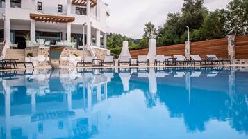 Una piscina con sillas de descanso y un edificio de fachada de piedra y terraza de madera.