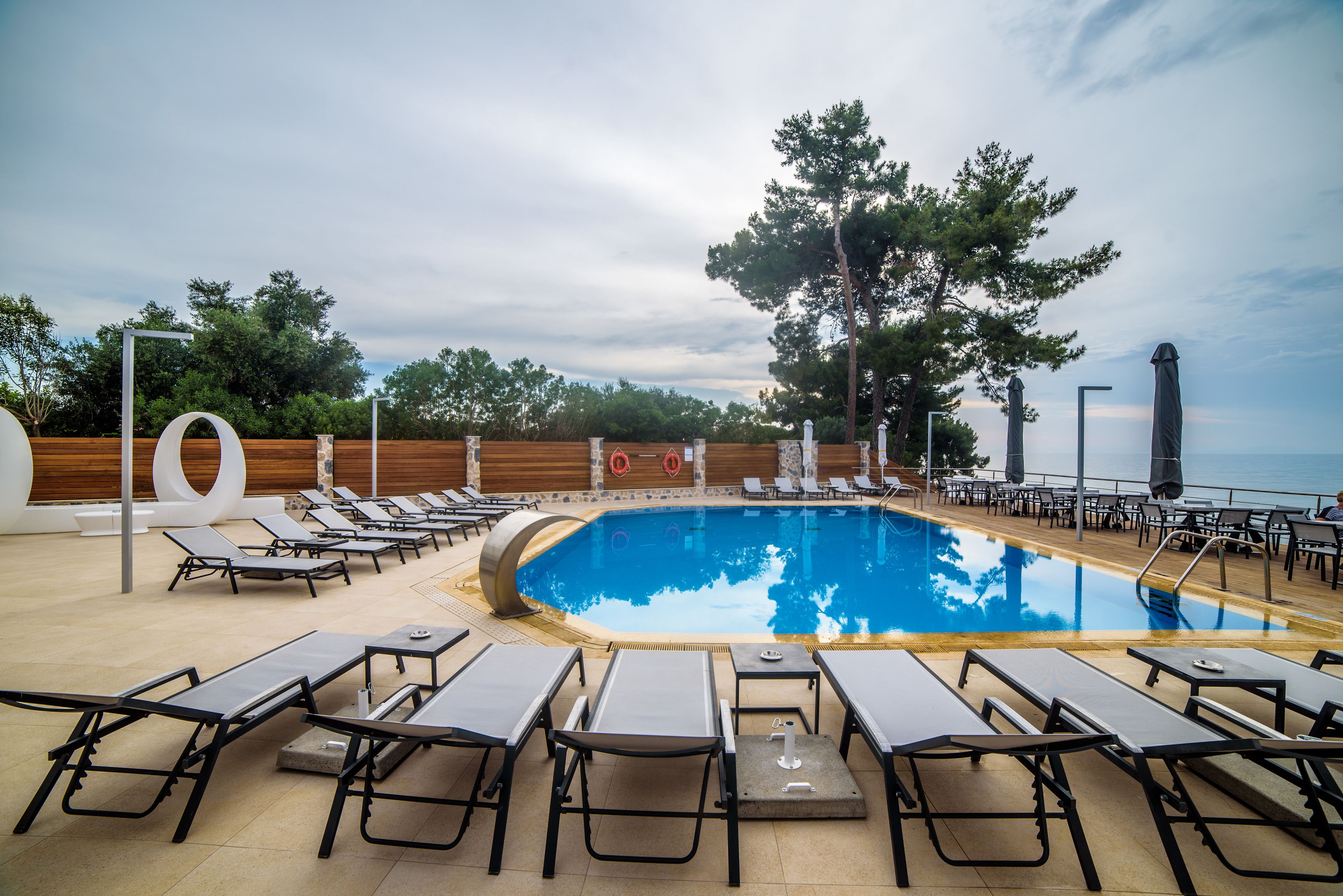 Uma área à beira da piscina com espreguiçadeiras, piscina e cerca de madeira.