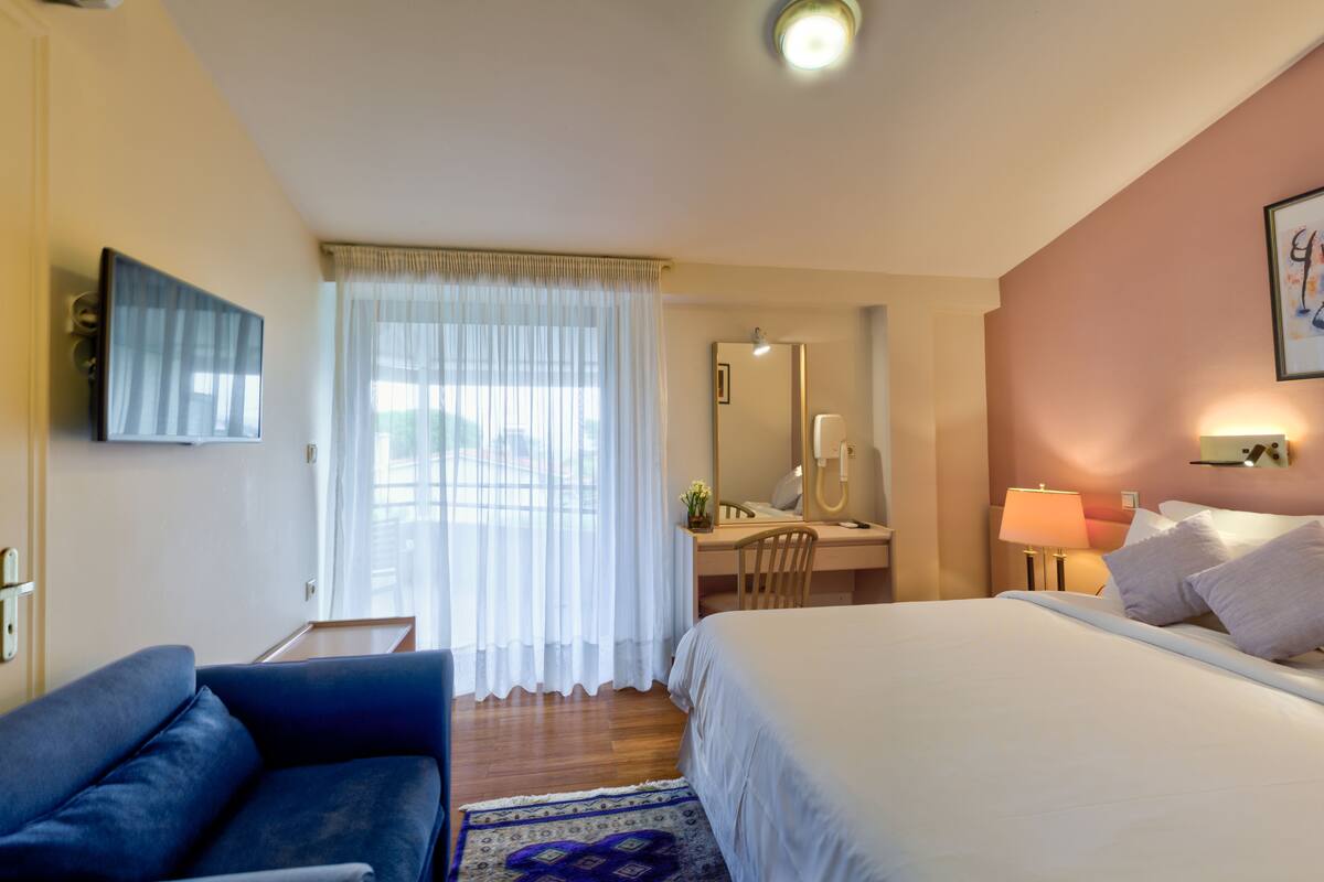 A hotel room with a bed, a desk, a chair, a TV, and a window with curtains.