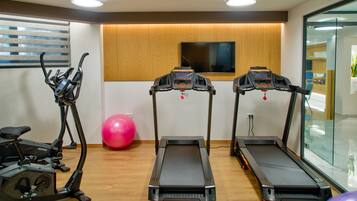 Un gimnasio con cintas de correr, bicicletas estáticas y una pelota de ejercicios grande.