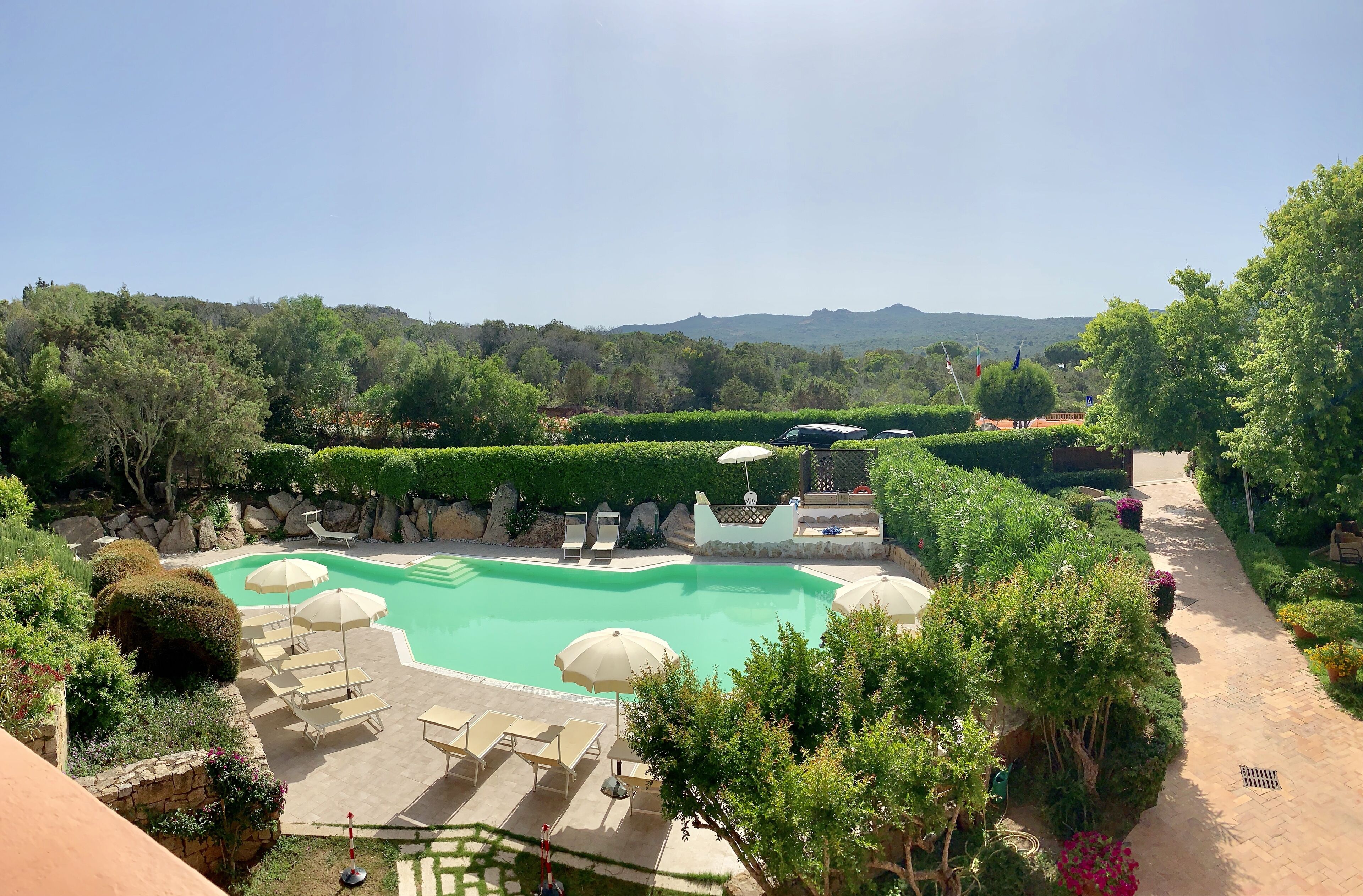 Una piscina con tumbonas y sombrillas, rodeada de jardines ajardinados y vistas a las colinas.