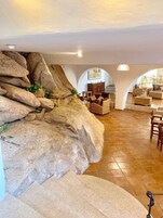 Un salón espacioso con una gran formación rocosa, muebles de madera y suelo de baldosas.