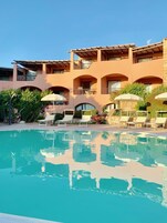 Un hotel con piscina, sillas de descanso y sombrillas.