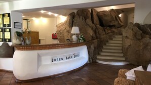 En receptionsdisk märkt med texten ”GREEN PARK HOTEL”, med en rustik stenmur som bakgrund och en trappa som leder upp till de övre våningarna.