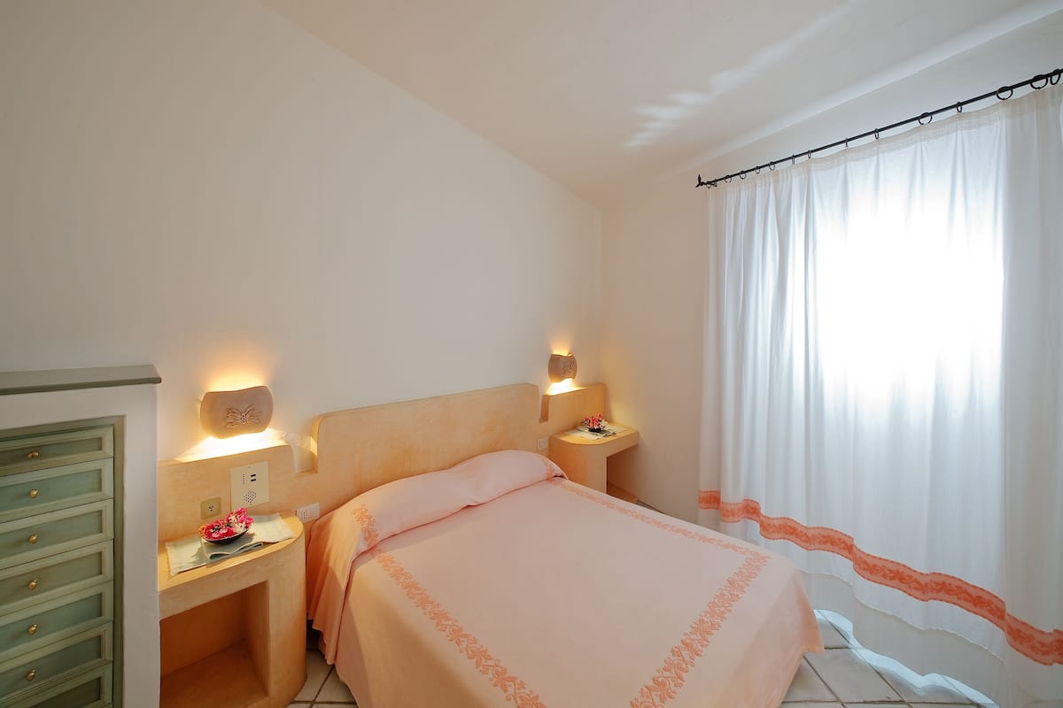 Una camera da letto con un letto, comodini, un tavolino, una cassettiera e una finestra con tende.