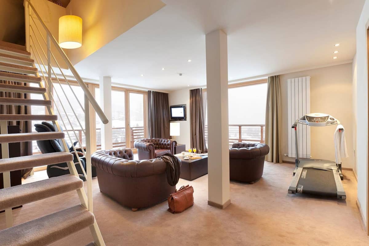 Un vaste espace de vie comprenant un escalier, des canapés en cuir, un tapis de course et un téléviseur.