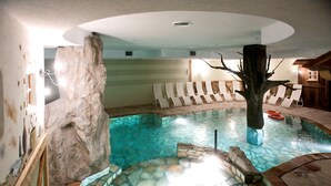 A circular pool with mosaic tiles, surrounded by lounge chairs and a stone wall. - Grand Hotel Paradiso (Ponte di Legno)