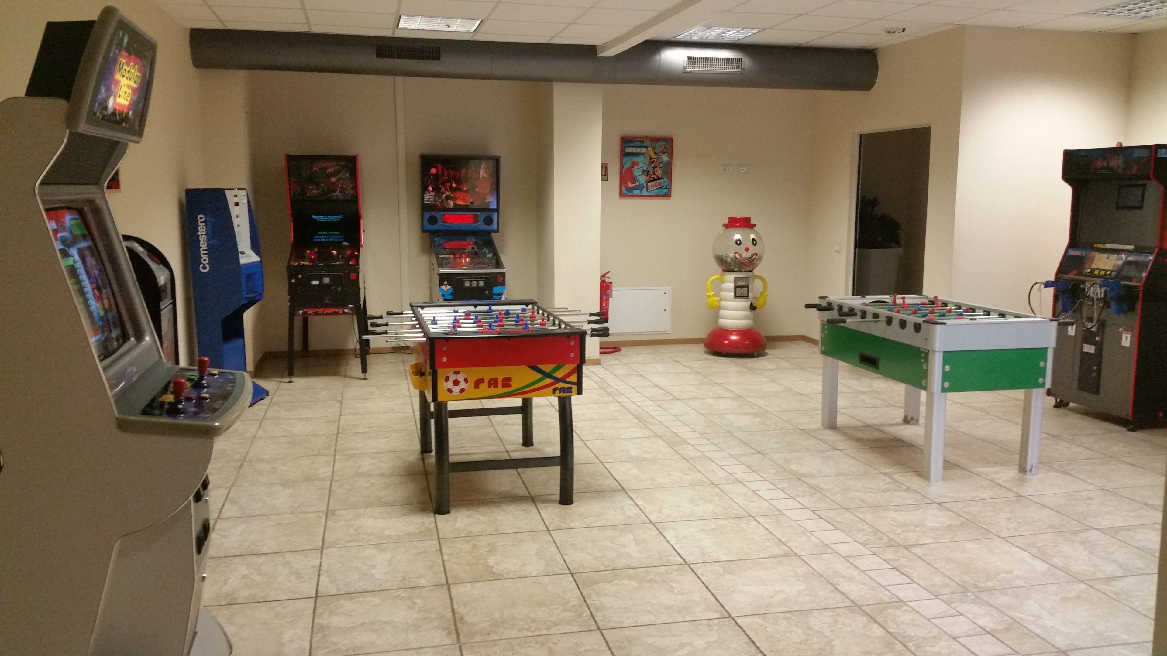 A room with two foosball tables, arcade games, and a vending machine.