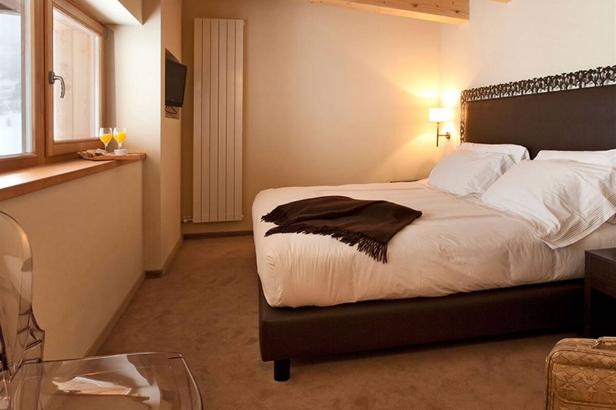 Une chambre à coucher comprenant un lit, une table de chevet, une lampe, une fenêtre, un radiateur et une chaise.