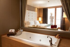 A hotel bathroom with a large bathtub, a mirror reflecting the room, and a window with curtains. - Grand Hotel Paradiso (Ponte di Legno)