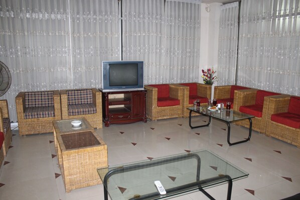 A living room with wicker furniture, a glass coffee table, and a television on a stand. - City Homes Hotel (Dhaka)