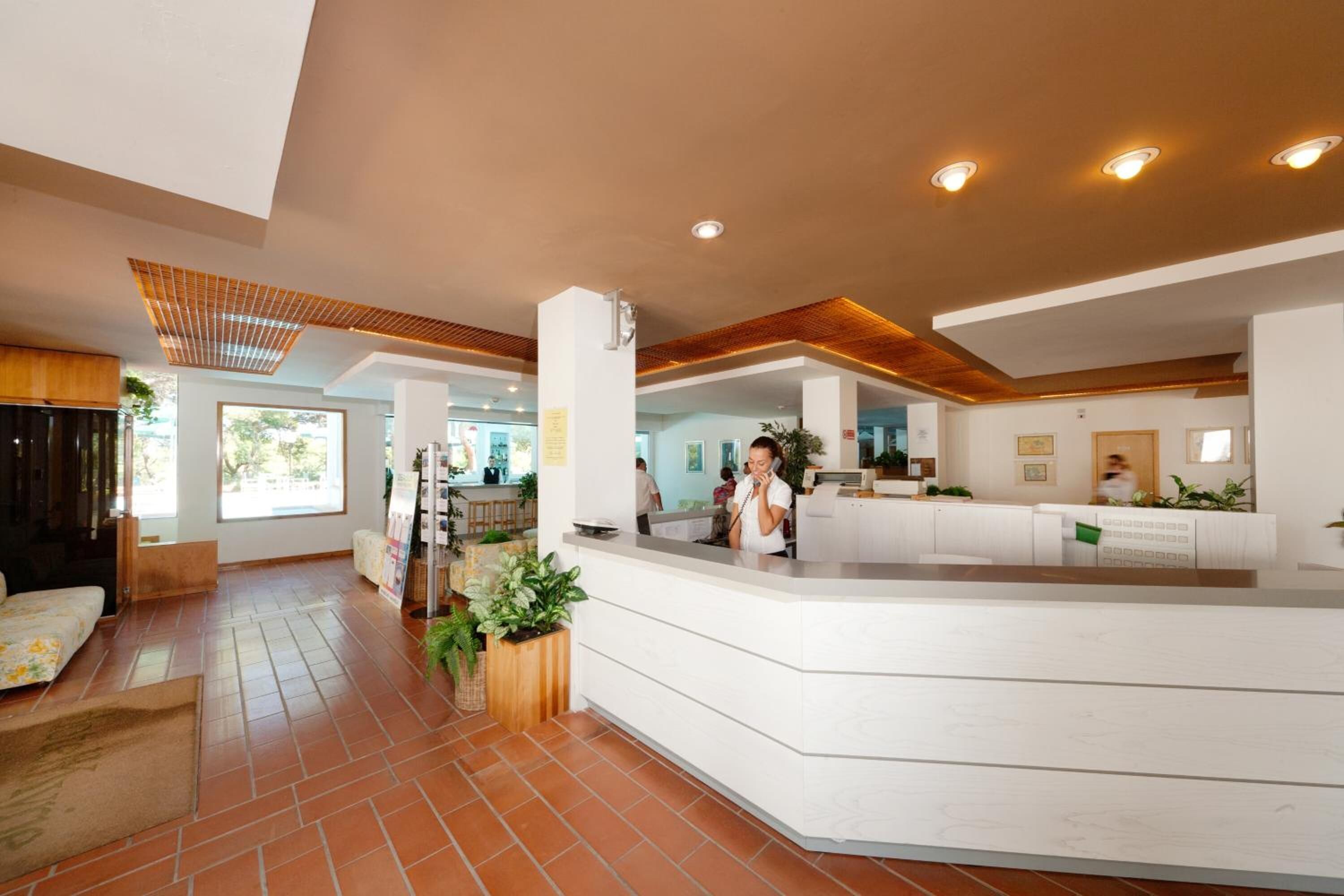 A modern hotel lobby with a reception desk, seating area, and large windows.