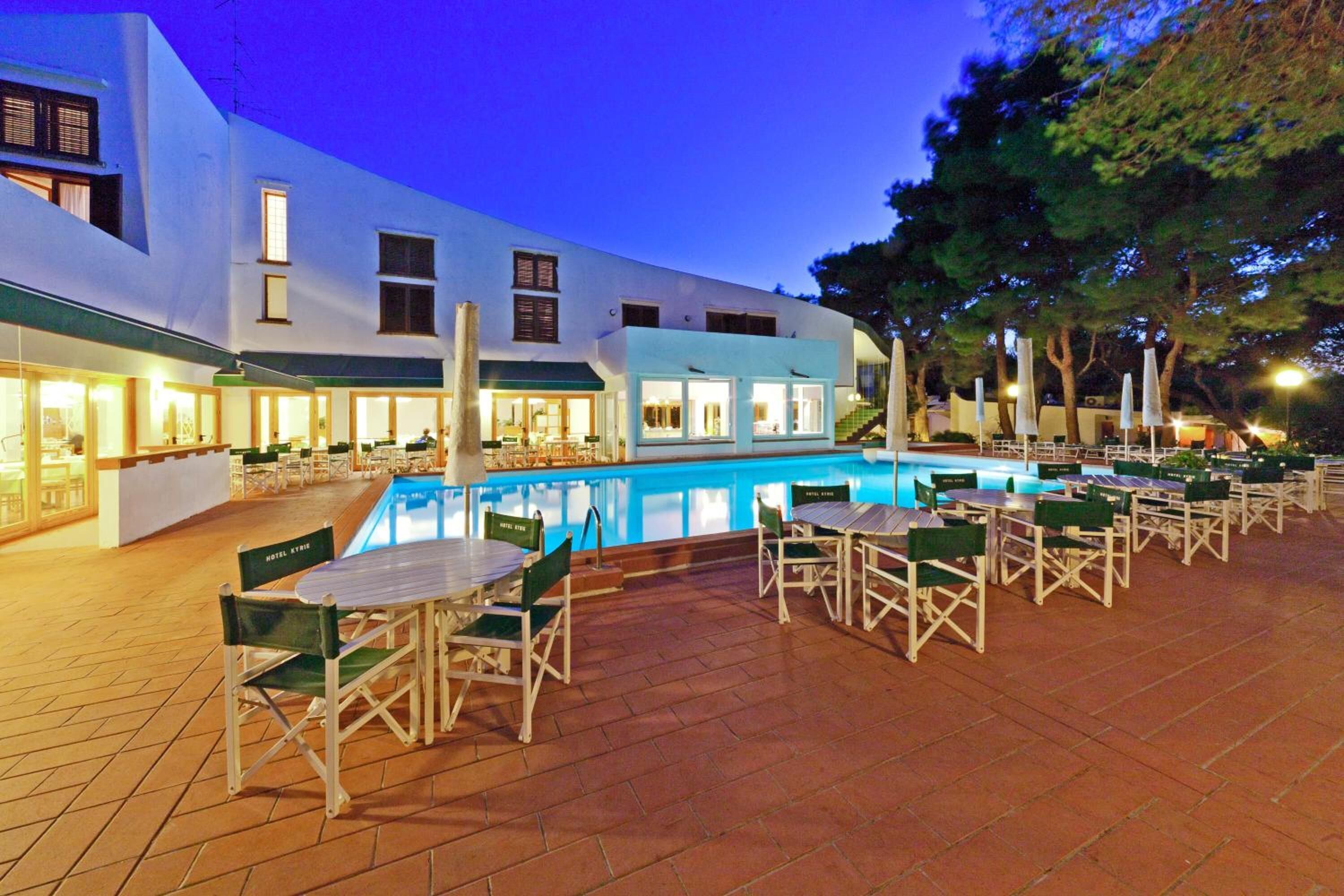 A hotel with a swimming pool, outdoor seating, and a white building facade.