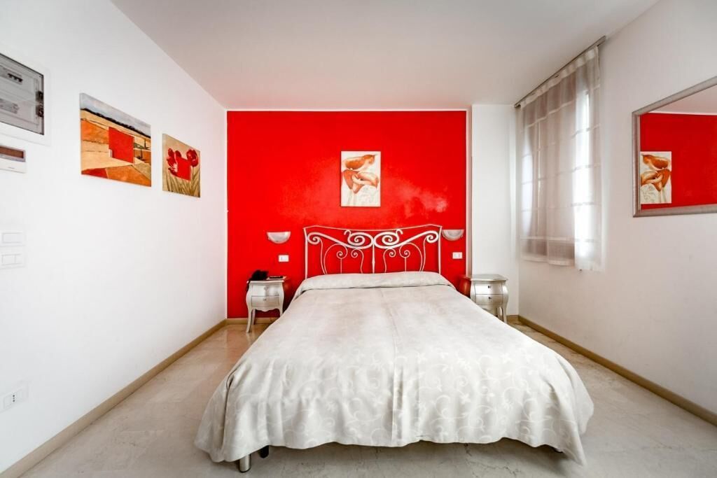 Un dormitorio con una pared de acento roja, una colcha blanca y un cabecero de metal.