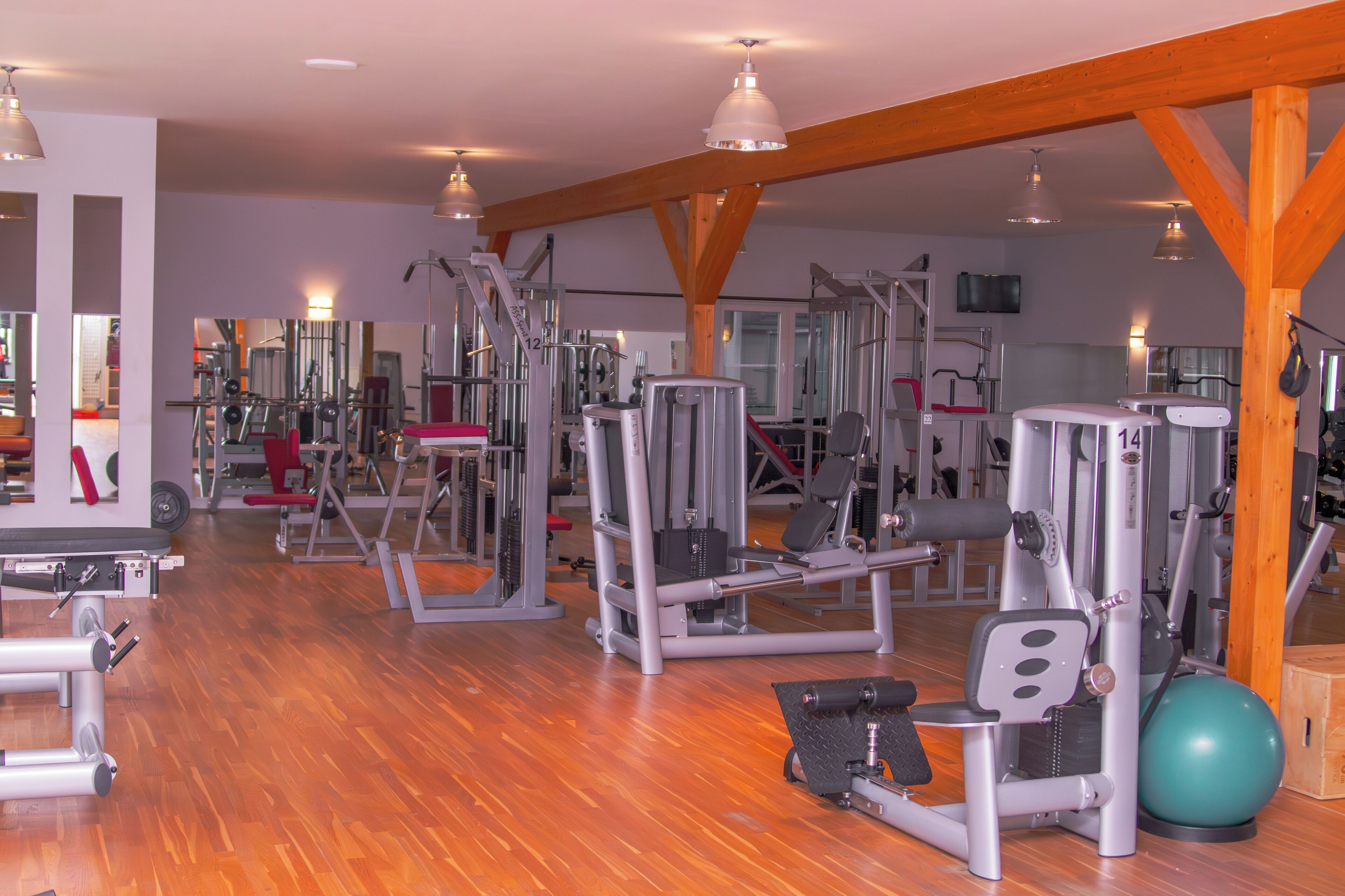A gym with various exercise machines, wooden beams, and a mirrored wall.