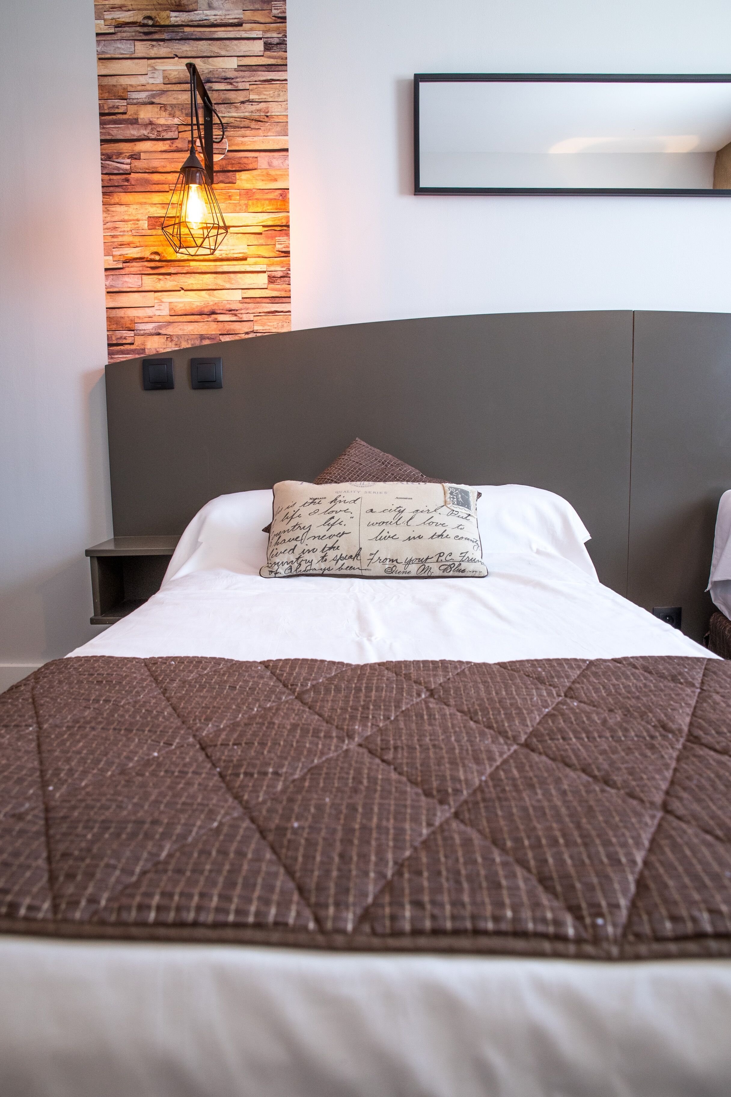 A neatly made bed with a brown quilted bedspread and a pillow with handwritten text.