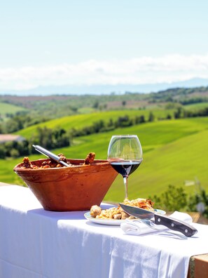 A table with a bowl of food, a wine glass, and a knife on a tablecloth with a scenic view in the background. - Auberge du Pastel (Nailloux)