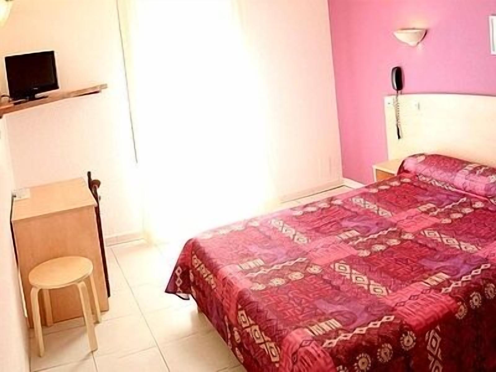 Un dormitorio con cama, escritorio, silla, teléfono y televisión.
