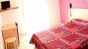 Un dormitorio con cama, escritorio, silla, teléfono y televisión.