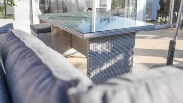 Un área de estar al aire libre con una mesa de vidrio y muebles de mimbre.