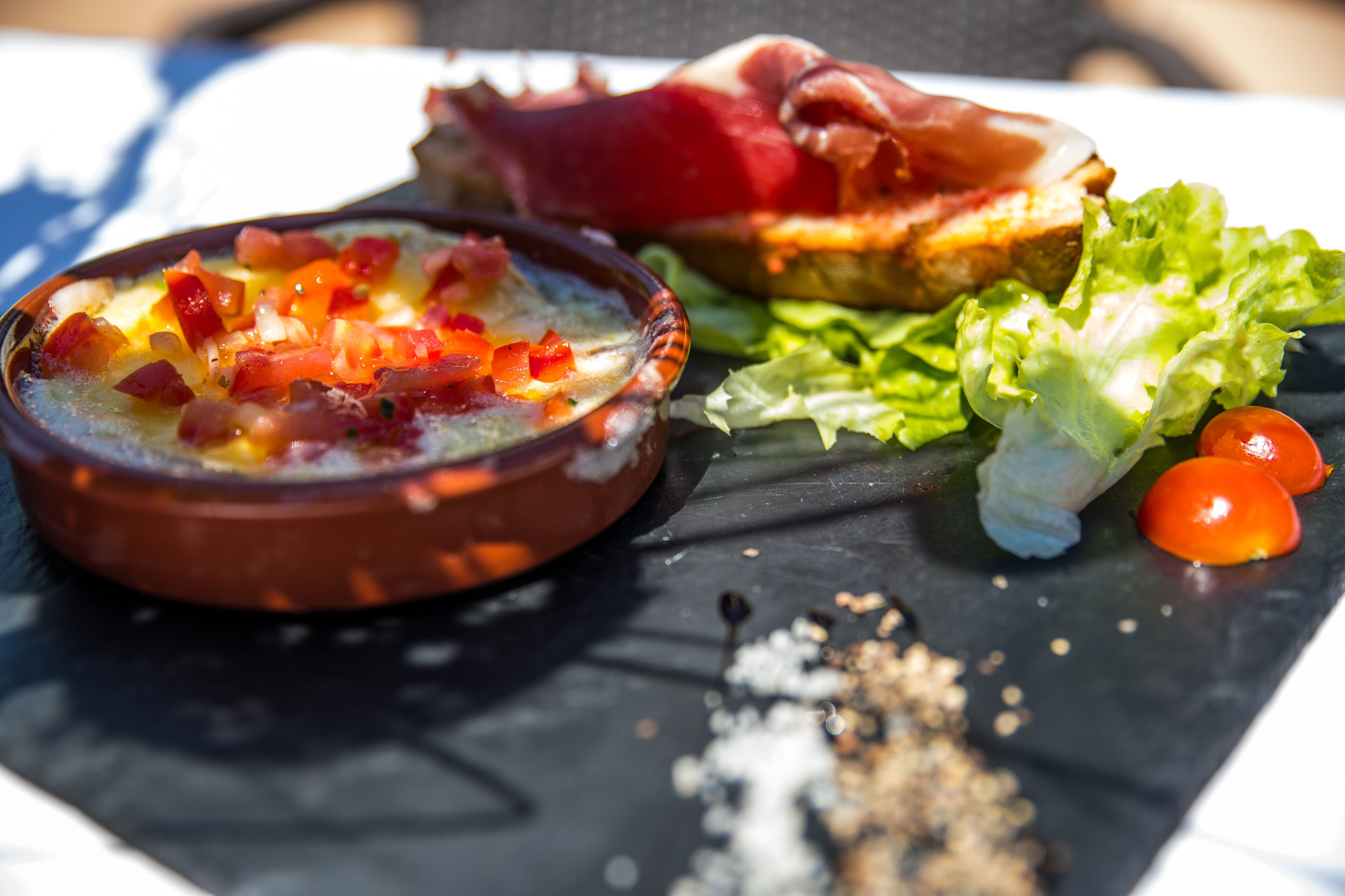 Un repas composé d’un bol de soupe, d’une tranche de pain et de quelques feuilles de laitue, le tout servi sur une assiette en ardoise.